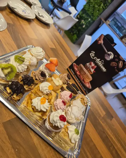 Bandeja de mini pasteles surtidos junto a carta, en La Artesana, Parla