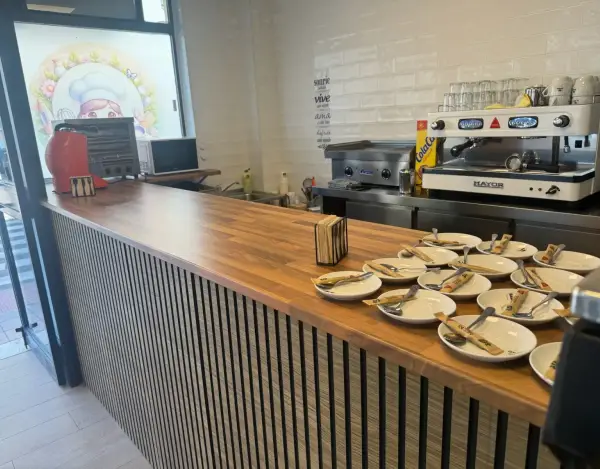 Barra de cafetería con cafetera y platos de churros, en La Artesana, Parla