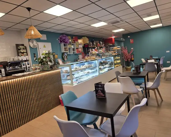 Interior de cafetería con mesas, barra y vitrinas, en La Artesana, Parla