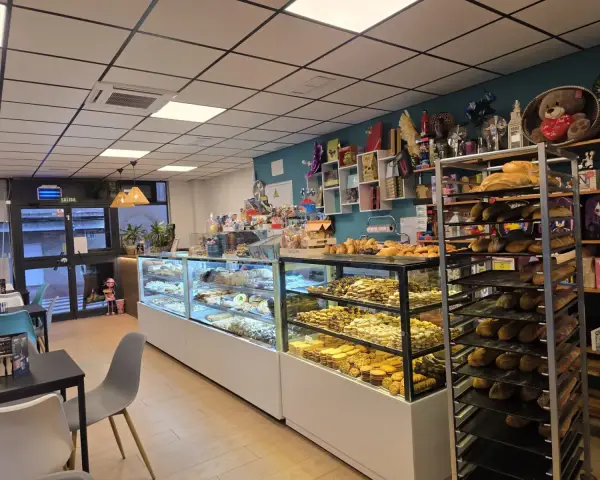 Interior con vitrinas llenas de dulces y mesas de cafetería, en La Artesana, Parla