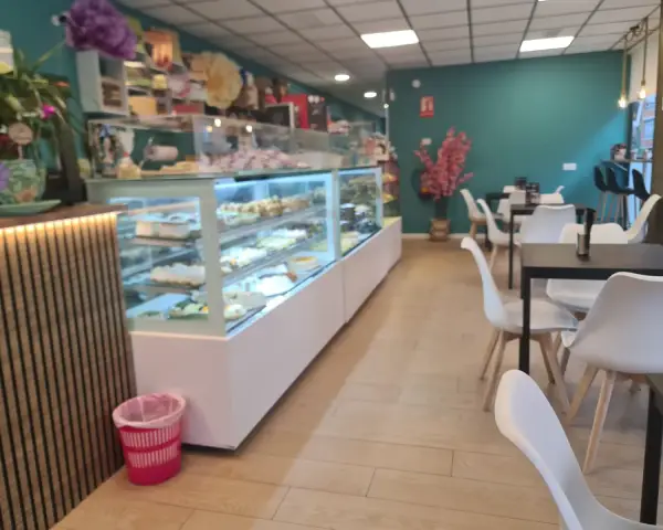 Interior con vitrinas de pasteles y mesas para clientes, en La Artesana, Parla