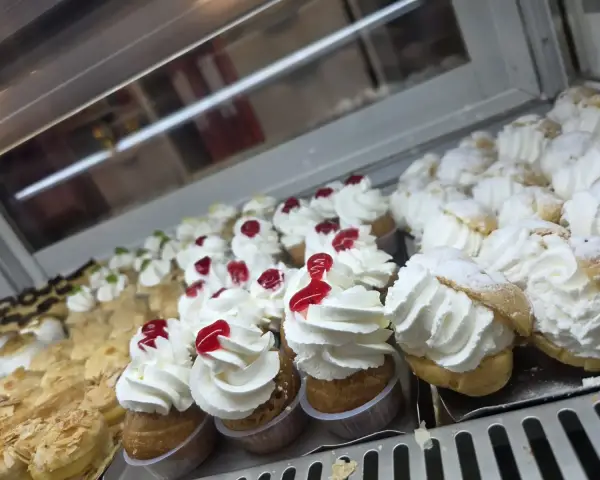 Profiteroles con nata y guinda en vitrina pastelera, en La Artesana, Parla