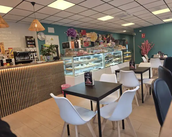 Salón de cafetería con mesas, barra y vitrinas dulces, en La Artesana, Parla