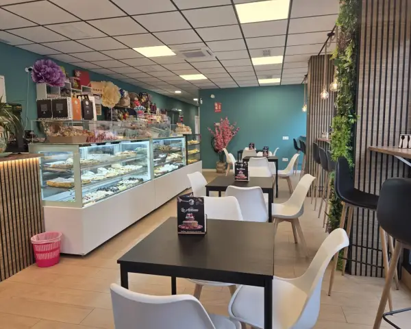 Salón interior con mesas y vitrinas de pastelería, en La Artesana, Parla